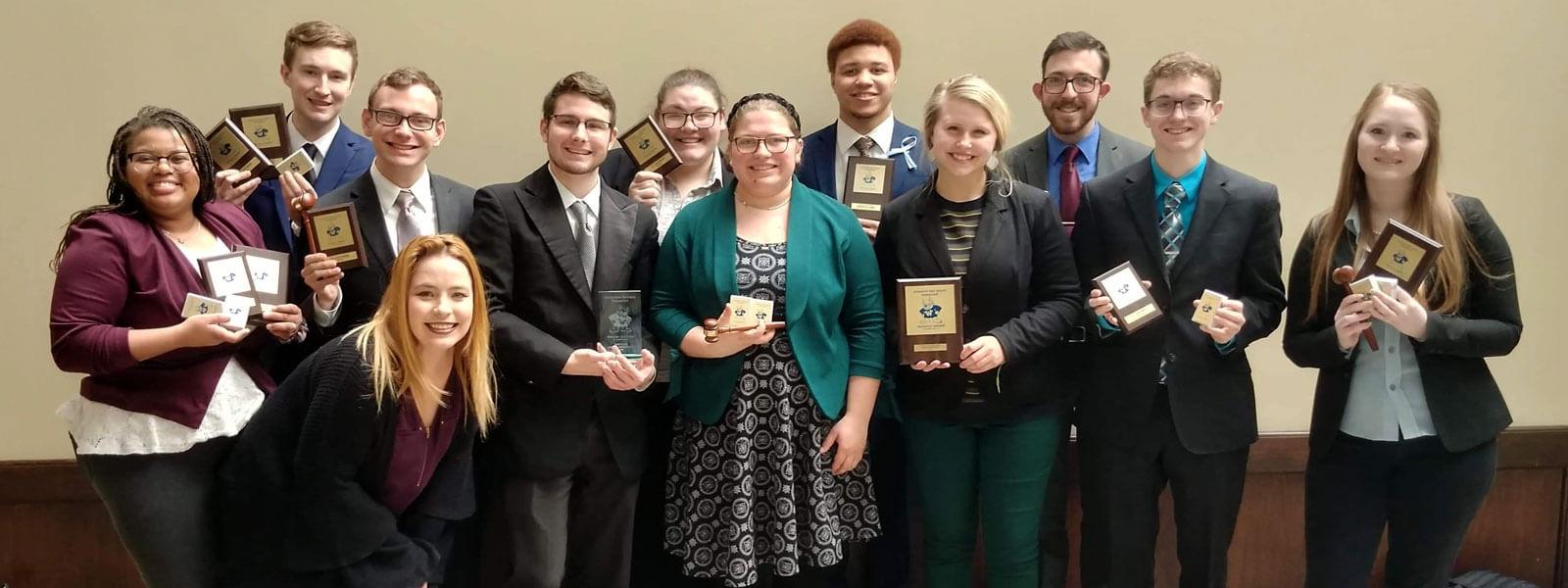 speech and debate team members pose with handfuls of trophies