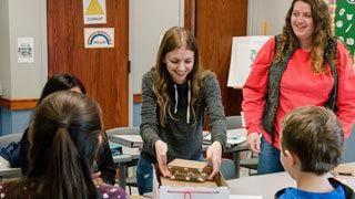 female college students smile while working on project with kids