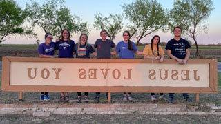 group of college students standing behind sign that says Jesus Loves you