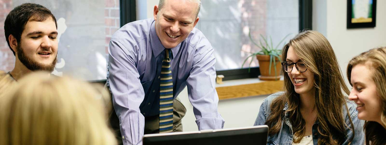 professor laughs with group of students working on project