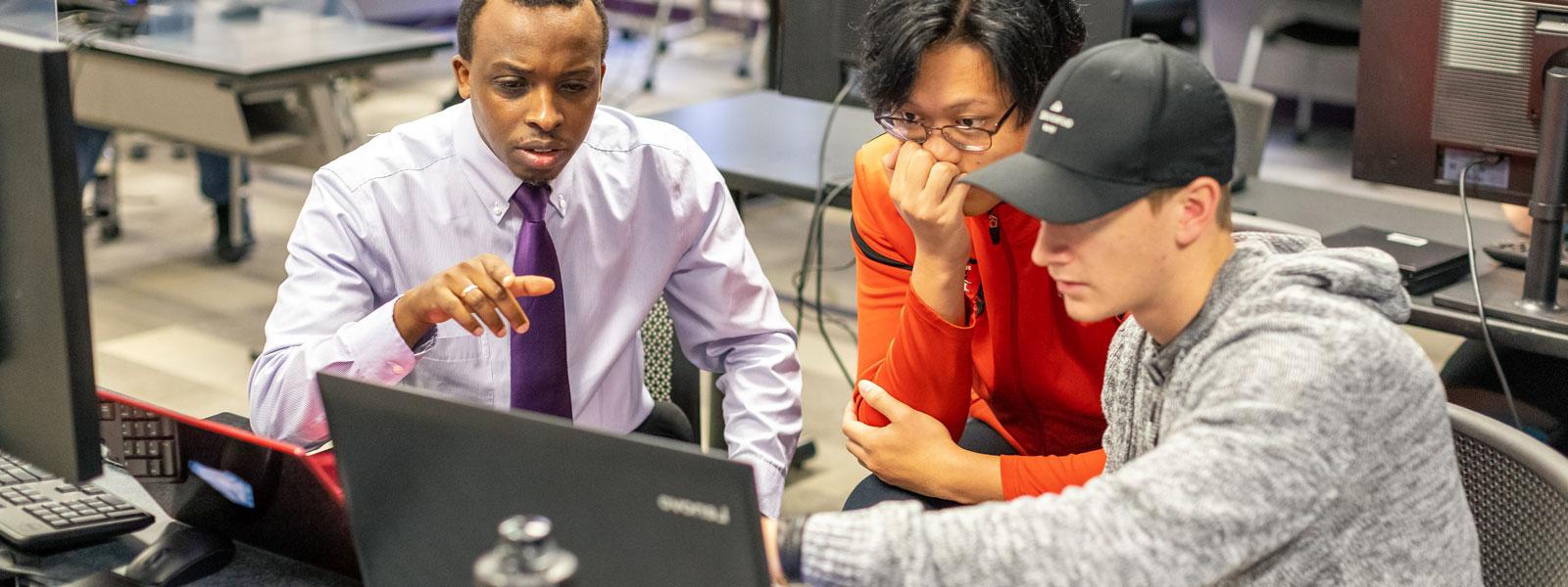 students work on laptops at tables in classroom