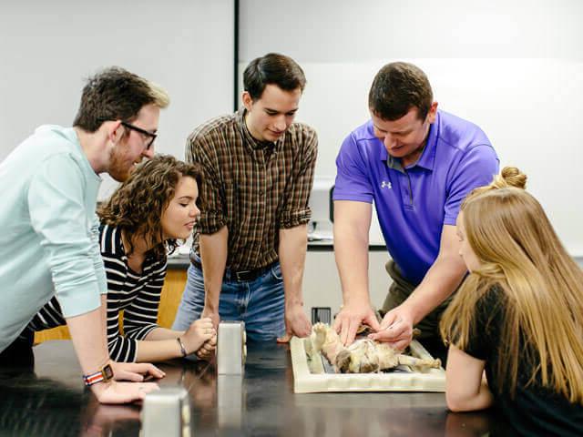 Professor and students gathered around anatomy mannequin