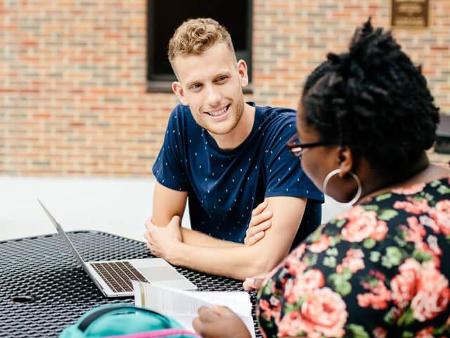 SBU students sitting at table outside with laptop between them